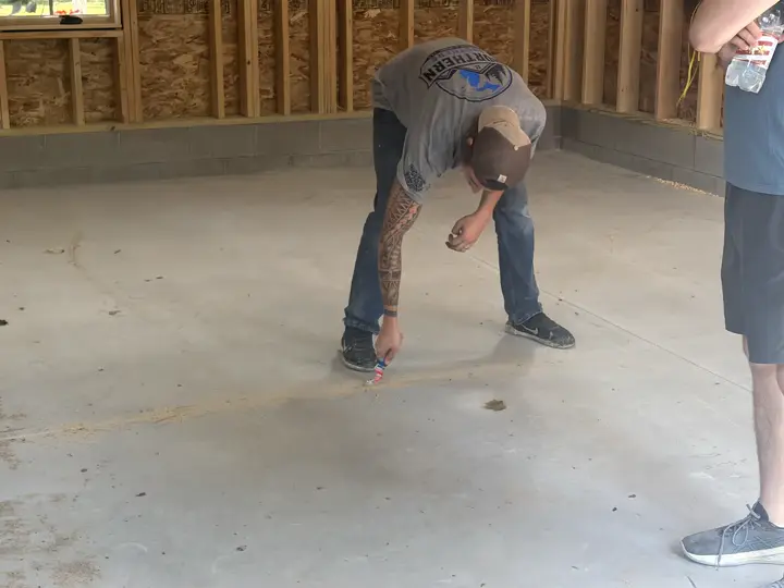 An installer crouches to inspect a bare concrete garage slab before coating